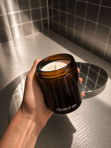 Amber glass scented candle in black-labeled jar, “OBJECT 01.” visible, held in hand