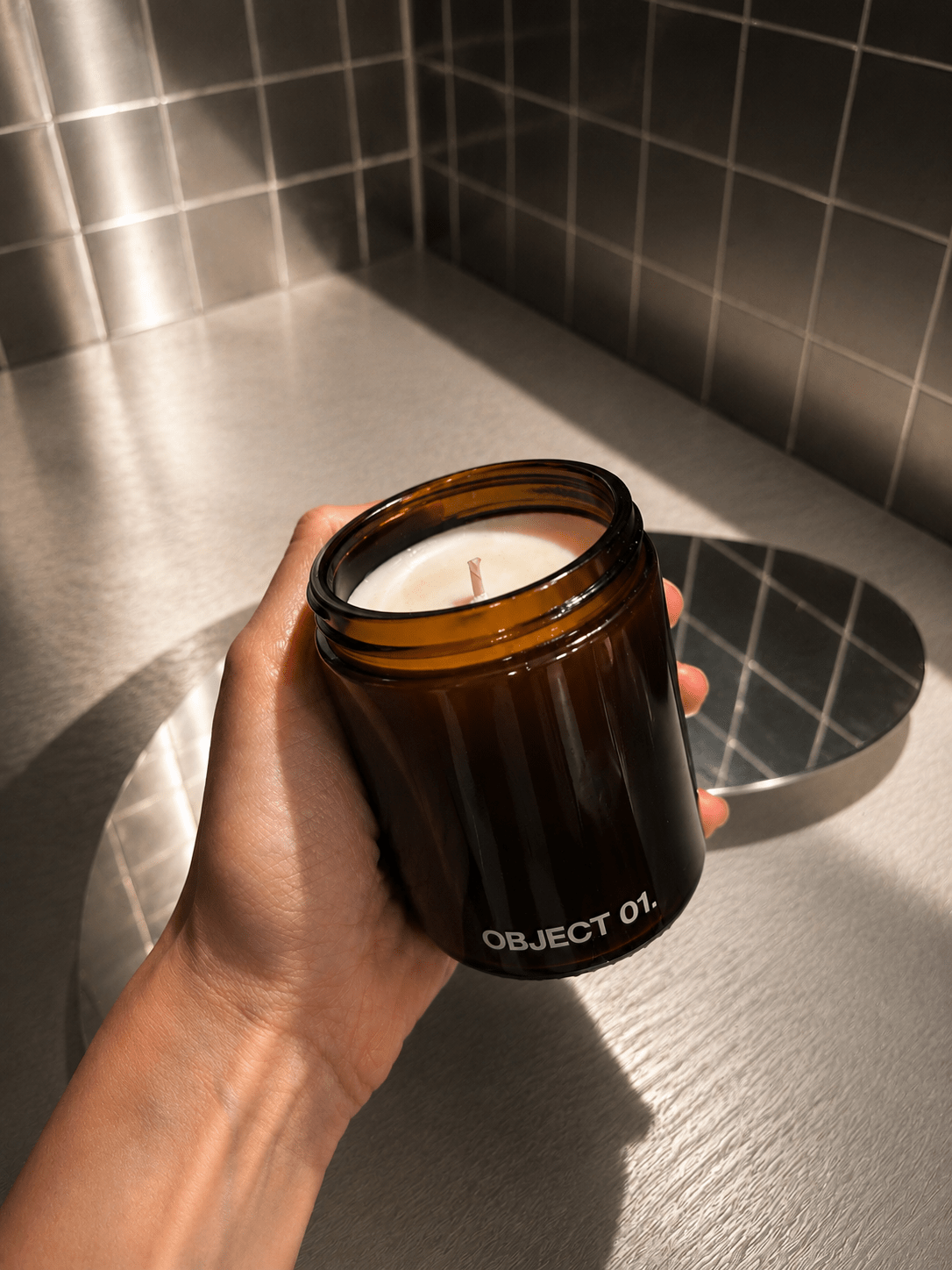 Amber glass scented candle in black-labeled jar, “OBJECT 01.” visible, held in hand