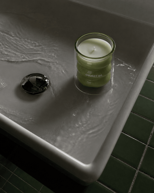 Green soy candle in glass jar on a countertop with a visible wick