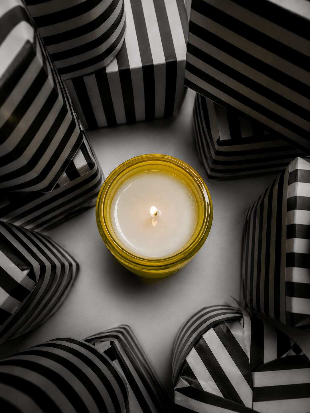 Scented candle in clear glass jar with golden wax and small flame.