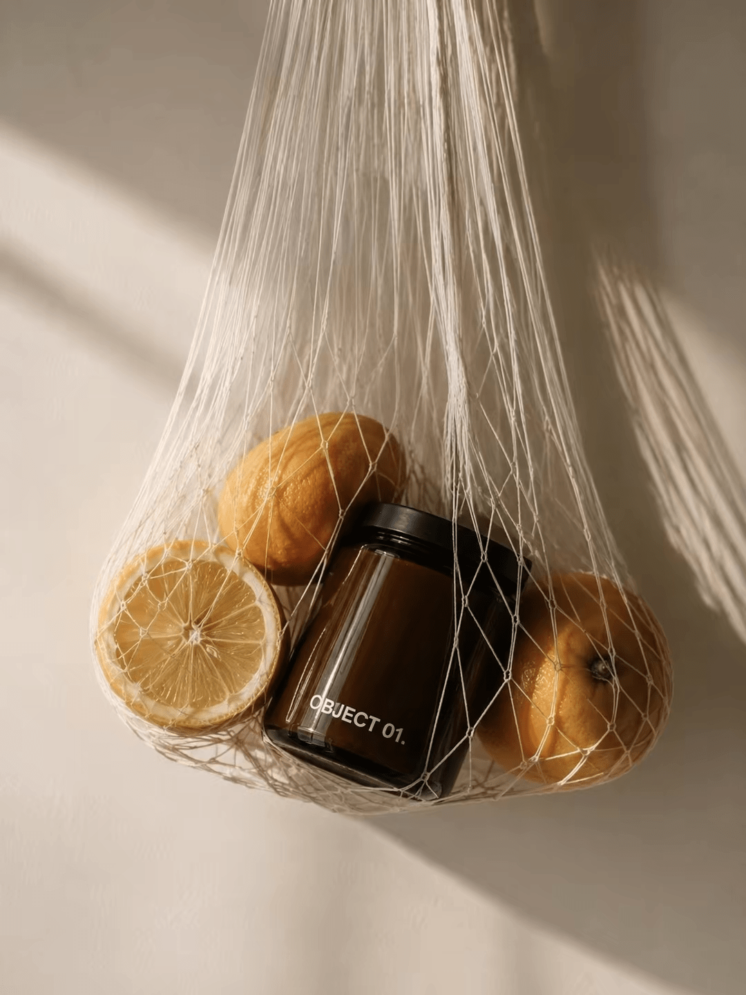 Dark amber glass scented candle jar in mesh bag with citrus.