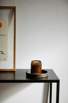 Amber glass scented candle jar with black base and lid, centered on a tray
