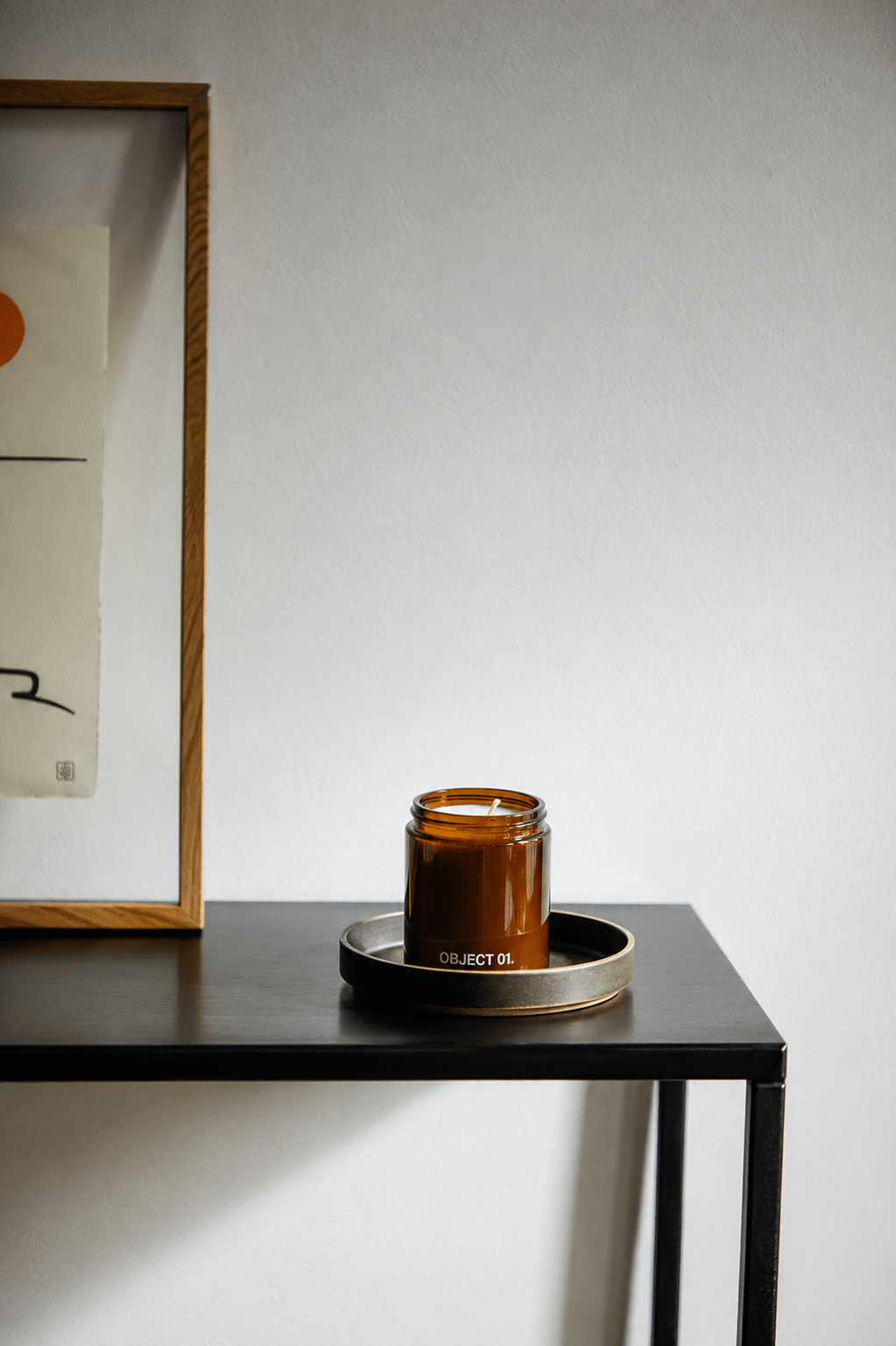Amber glass scented candle jar with black base and lid, centered on a tray