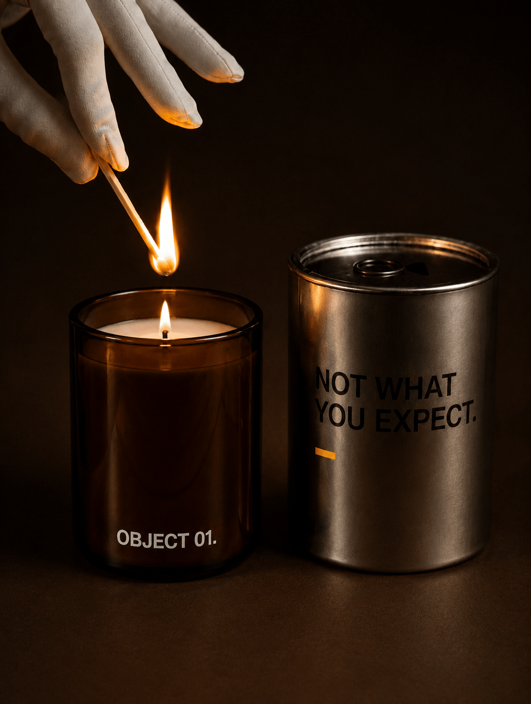 Lit amber jar candle and lit silver tin candle; hand lights the flame; label shows text
