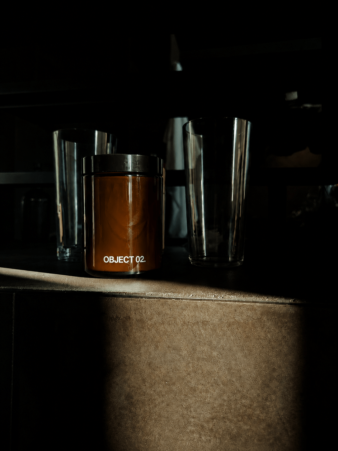 Amber glass scented candle jar with black lid, OBJECT 02 label on metal base