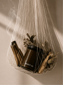 Scented candle in amber glass jar with visible flame and dried botanical accents