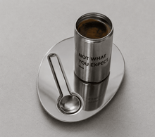 Stainless candle tin on saucer with spoon; text "NOT WHAT YOU EXPECT."