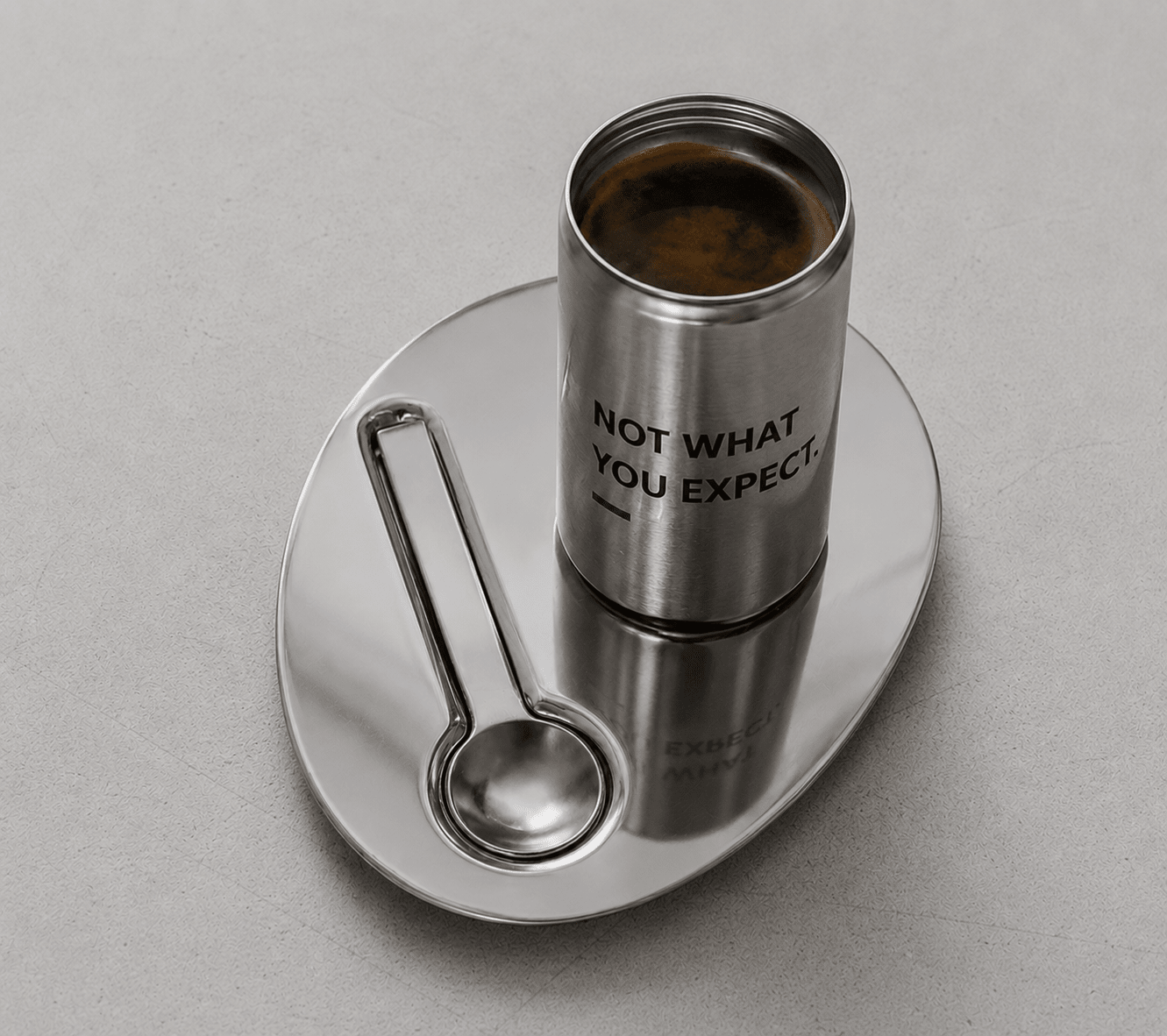 Stainless candle tin on saucer with spoon; text "NOT WHAT YOU EXPECT."