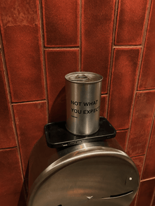 Metal scented candle tin on black holder with label "NOT WHAT YOU EXPECT."