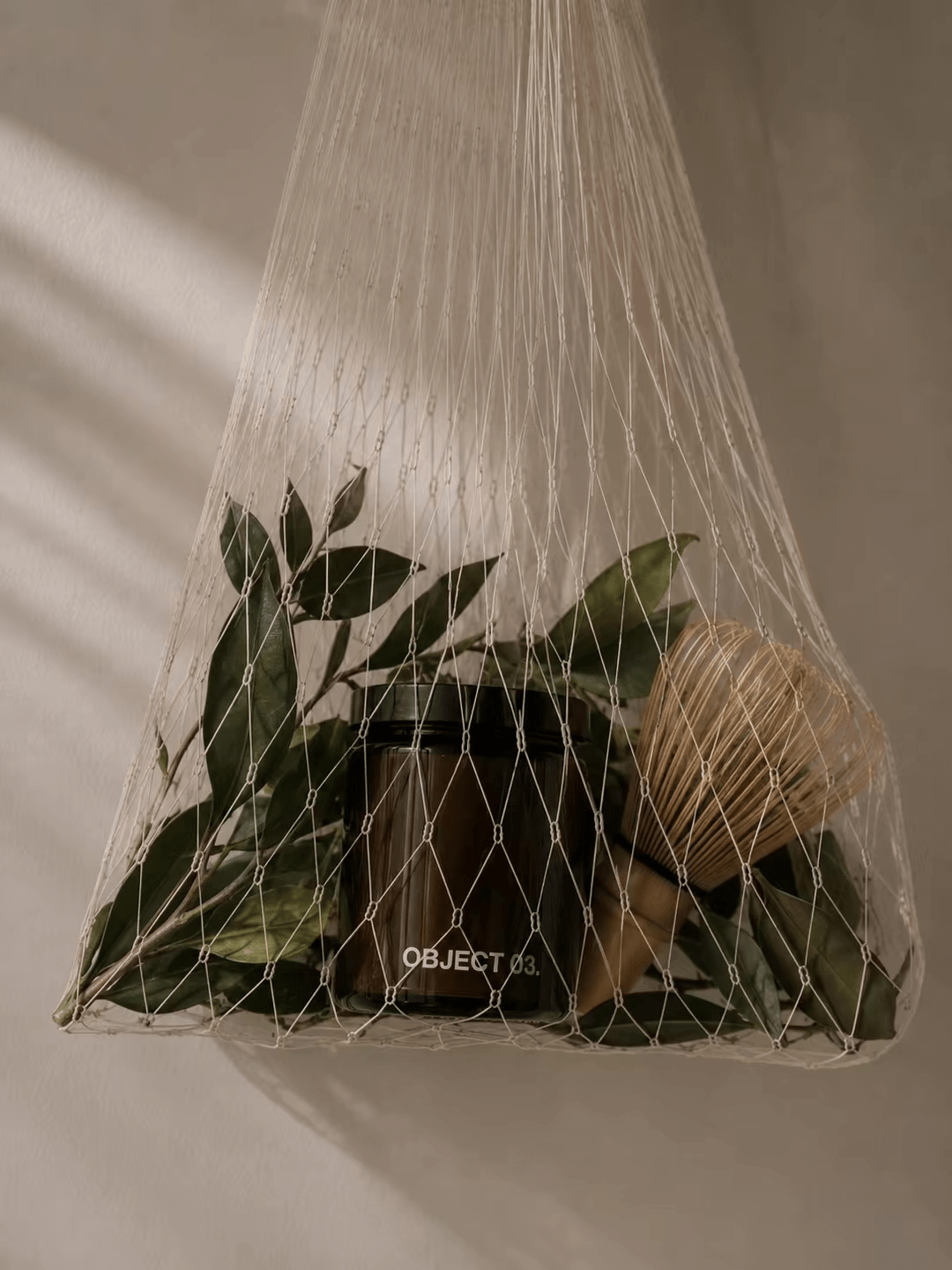 Net-wrapped scented candle with greenery and twine, jar visible under mesh