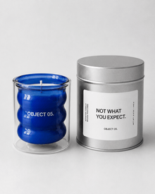 Blue glass OBJECT 05 candle beside a silver metal tin with a printed label.