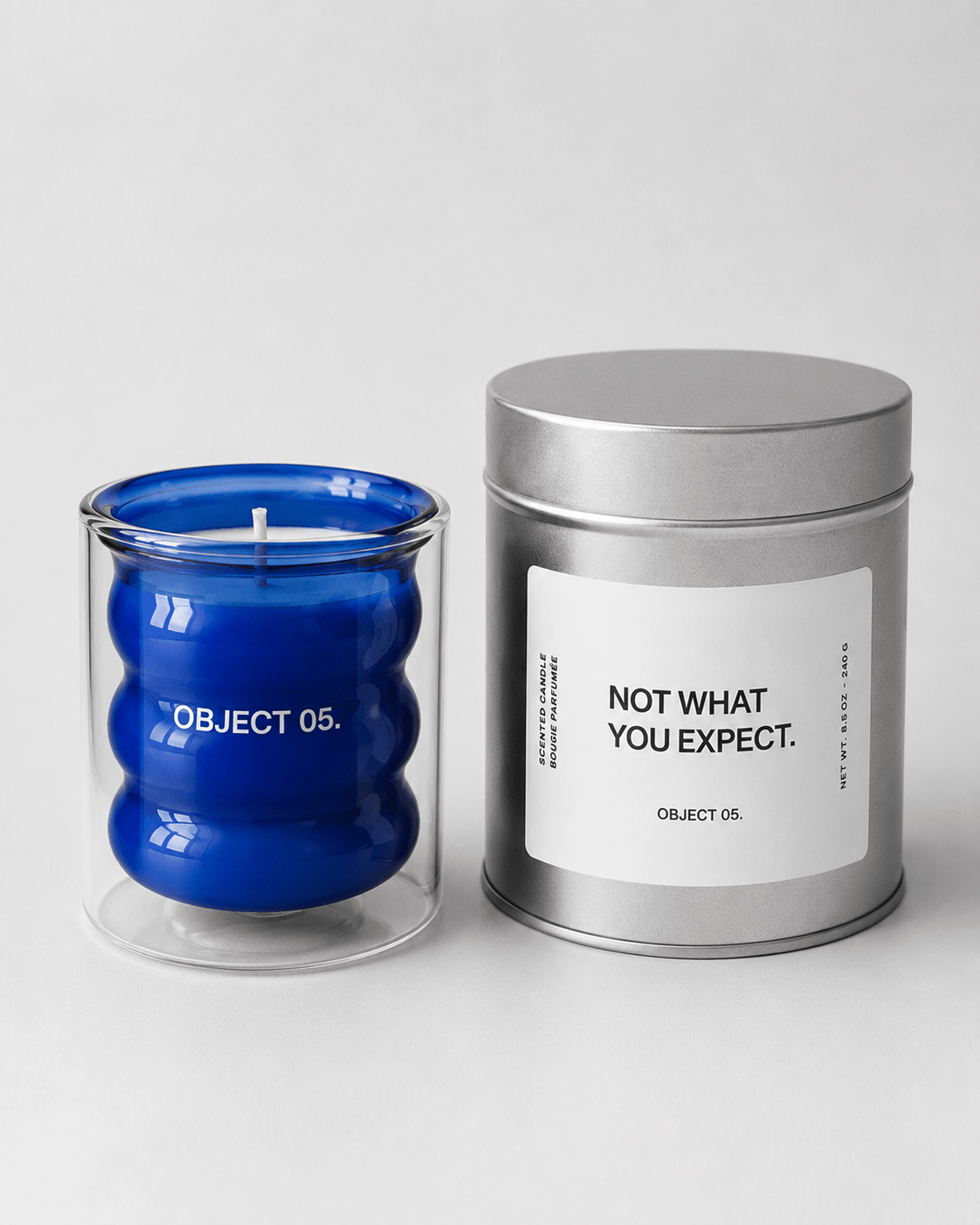 Blue glass OBJECT 05 candle beside a silver metal tin with a printed label.