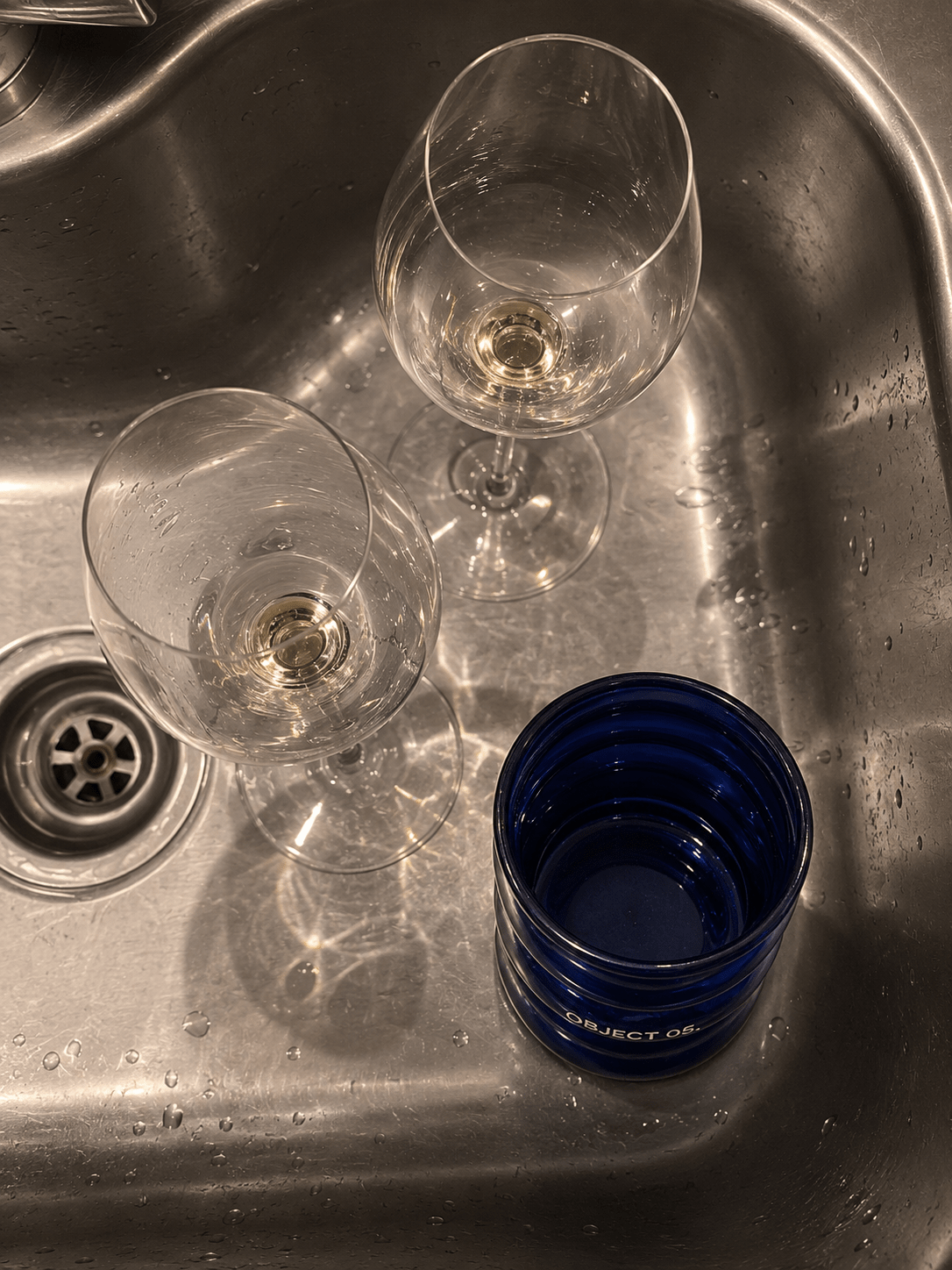 Blue glass candle jar on a metal sink with clear glasses around it