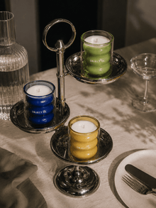 Colored glass candle jars with wicks: blue, green, and yellow on a dark tray