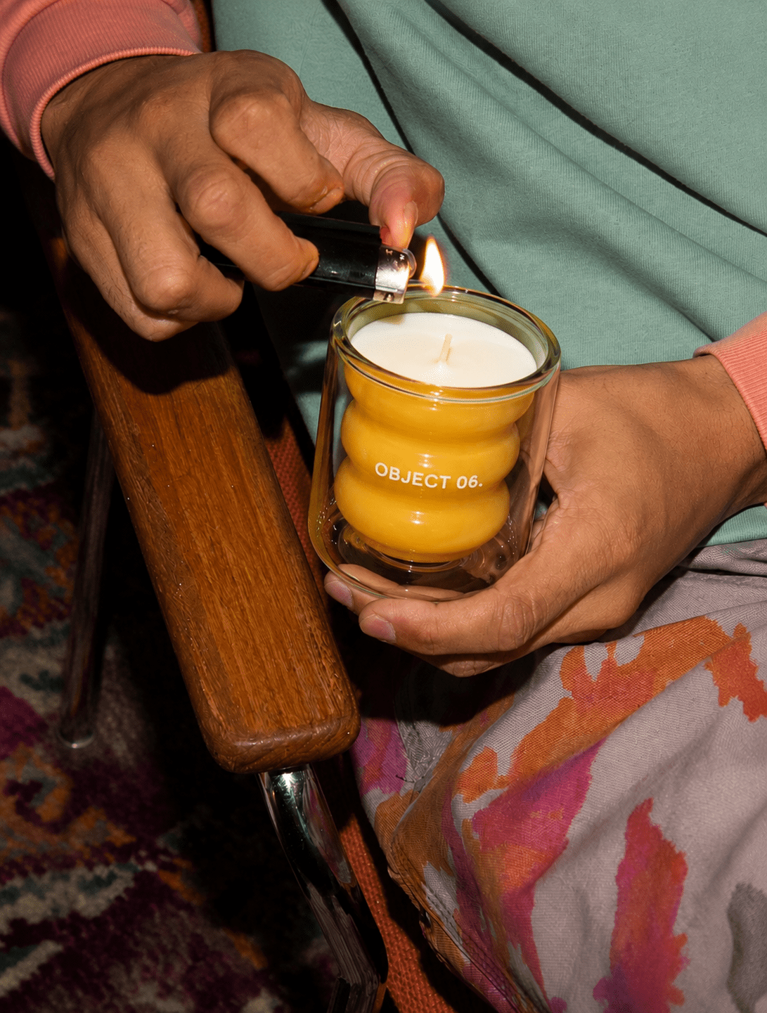 Scented candle in clear glass jar with golden wax, being lit by hand.
