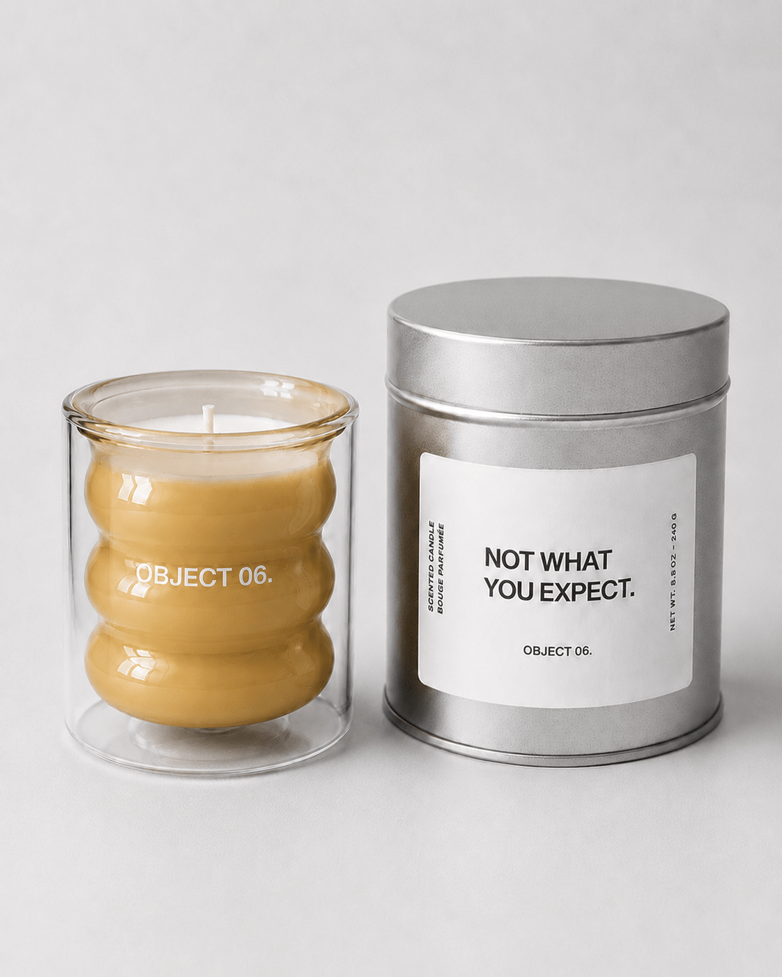 Scented candle set: yellow wax glass jar and silver tin with 'NOT WHAT YOU EXPECT' label